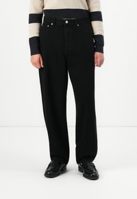 Schwarze weit geschnittene Denimhosen mit hoher Taille, ausgestattet mit Fronttaschen und silbernen Hardware-Details. Glatte Textur und zeitloses Design.
