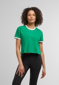 Zielony krótki t-shirt o jednolitej fakturze, z białą kontrastującą ribbową obróbką dekoltu i rękawów. W połączeniu z czarnymi legginsami.