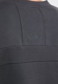 Maglione grigio scuro a maniche lunghe con tessuto texturizzato, con il logo in rilievo "The North Face" sulla spalla sinistra.