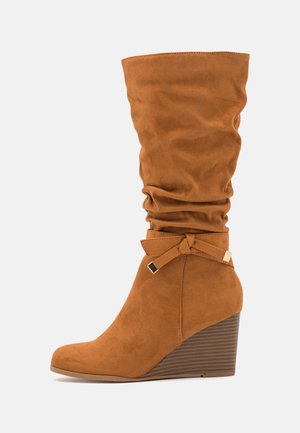 Botte compensée en daim marron avec un tige décontractée, un accent noué à la cheville et une semelle en wedge texturée.