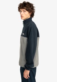 Fleece-pullover med hög krage; har en marinblå övre del och en ljusgrå nedre del. Mjuk textur med minimal branding.