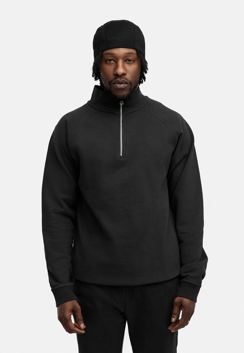 Schwarz, mit Reißverschluss, Fleece-Pullover mit hohem Kragen und Raglanärmeln. Hergestellt aus einem weichen Material, mit einem schmalen Reißverschluss am Hals.