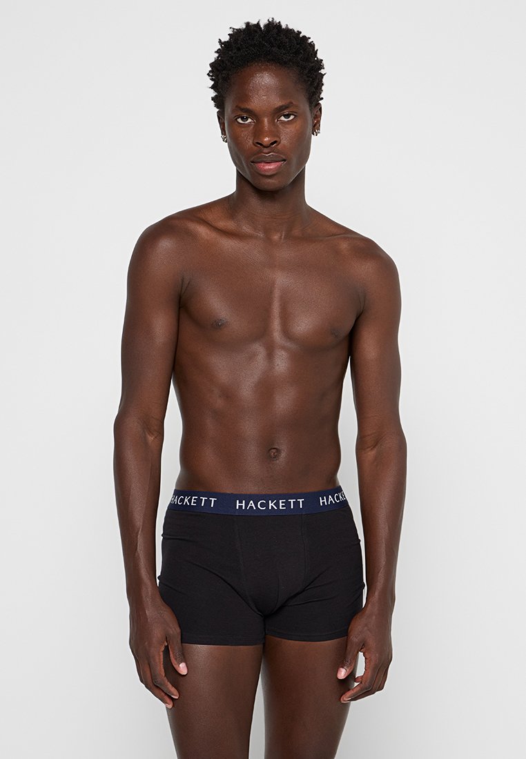 Boxer ajustados de algodón negro con una cinturilla azul marino que presenta el logo "HACKETT". Textura suave, diseño ceñido y longitud hasta el muslo.