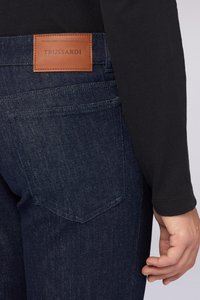 Mörkblå denimjeans med en brun läderlapp märkt "TRUSSARDI", med två bakfickor och en slät textur.