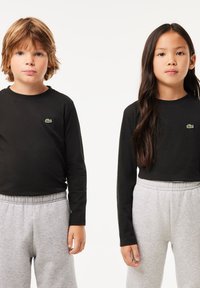 Magliette a maniche lunghe nere con un logo verde, abbinate a pantaloni grigi chiari con vita elastica, indossate da due bambini che stanno in piedi fianco a fianco.