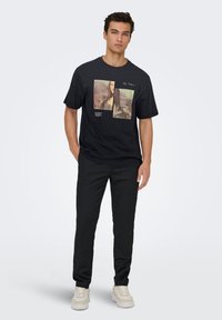 Sort t-shirt med grafisk print af Mona Lisa og tekst. Kombineret med sorte bukser og lyse sneakers.