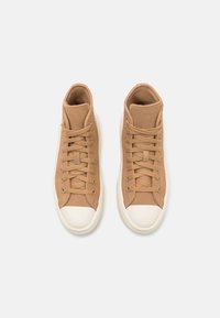 Beige hoge sneakers met een gestructureerde suède bovenkant, crèmekleurige veters en een witte rubberen neuskap, met een eenvoudig, minimalistisch ontwerp.