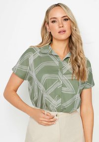 Korte mouwen knoopshirt in olijfgroen, met een geometrisch wit patroon. Zachte stof met een kraag en een getailleerde pasvorm.
