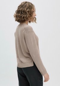 Beiger Strickpullover mit Rundhalsausschnitt, gerippten Bündchen und Saum, mit lockerer Passform und subtiler Textur. Getragen mit schwarzen Hosen.