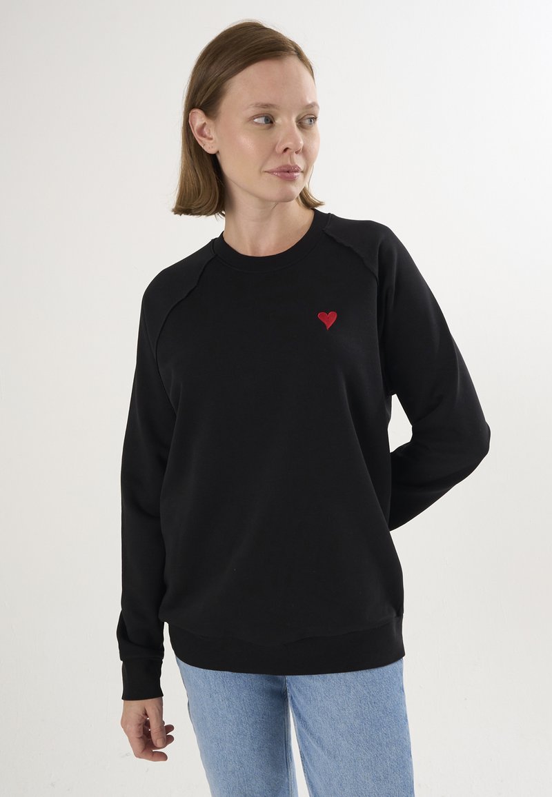 Must mustreid raglan varrukkade ja väikese punase südame tikandiga rinnas. Valmistatud pehmest, tekstuuriga kangast.