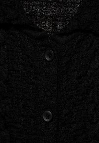 Cardigan en tricot noir avec un motif texturé et une large fermeture à bouton. Le tissu a une apparence douce et pelucheuse.