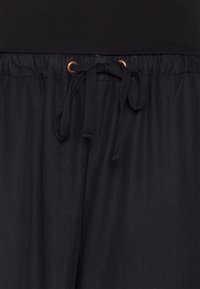 Pantalons noirs à taille élastique avec une texture lisse, dotés d'une fermeture à cordon et d'œillets en métal doré pour l'ajustement.