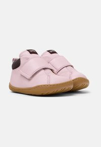 Zapatos de cuero rosa con una correa de velcro, que presentan un acento marrón en el talón y una suela de goma flexible color beige con ranuras texturizadas.