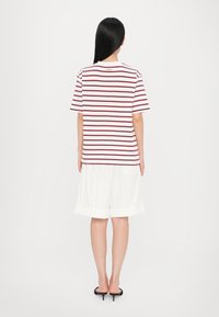 Stribet t-shirt i hvid og bordeaux, korte ærmer, afslappet pasform. Sat sammen med løse hvide shorts. Glat tekstur, afslappet design.