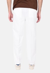 Pantaloni bianchi su misura con una linea dritta, tasche posteriori e una texture liscia, abbinati a calzature beige con accenti blu.