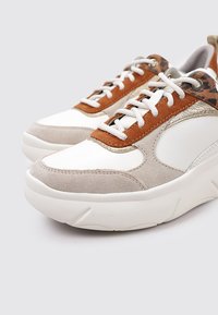 Sneakers che presentano una combinazione di pelle bianca, suede beige e pelle marrone con un accento metallico, punta rotonda e suola in gomma spessa.