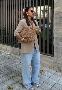 Beige oversized blazer, ljusblå vida jeans, vita sandaler och en texturerad halmkhash. Tillbehör inkluderar guldörhängen och armband.