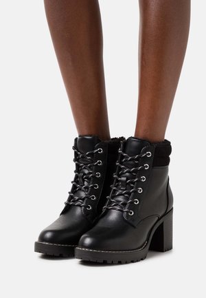 Bottes noires en cuir avec un bord en fausse fourrure, design à lacets, œillets en métal argenté et un large talon bloc. Semelles texturées pour une meilleure adhérence.