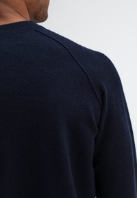 Navyblauw gebreid trui met een ronde hals, geribbelde manchetten en een zachte textuur, met een zichtbare schoudernaden detail.