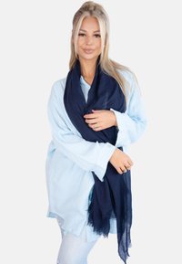 Écharpe texturée bleu marine en tissu léger, drapée sur les épaules, complétée par une chemise à boutons bleu clair.