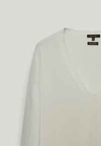 Maglione bianco in cotone a V con maniche lunghe; presenta una sottile texture a coste e linee pulite per un design semplice e classico.