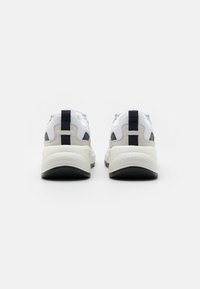 Weiße Sneakers mit grauen und marineblauen Akzenten, ausgestattet mit einem strukturierten Obermaterial, gepolstertem Kragen und einer dicken Gummisohle. Branding am Absatz.