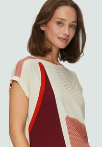 Korte mouw, top met abstracte patronen in crème, met bordeauxrood, koraal en stippenontwerpen. Het heeft een relaxte pasvorm en een zachte textuur.