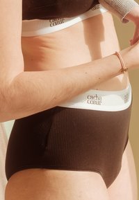 Melnas ribotas apakšveļas komplekts ar baltu jostu, kurā ir izdrukāts "cache cœur" brūnā krāsā. Gluda tekstūra, augstās vidukļa dizains.