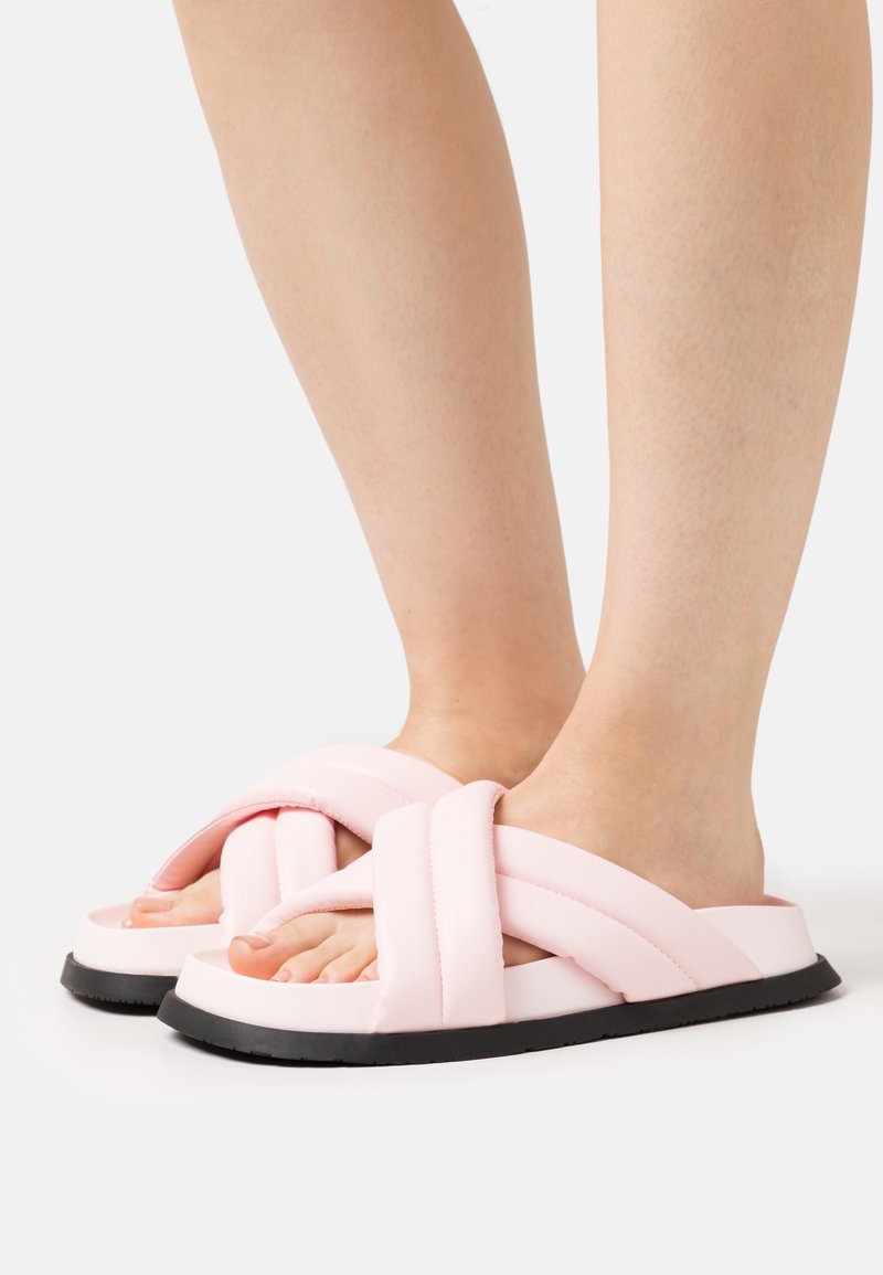 Sandales roses à enfiler avec des lanières épaisses en design croisé, dotées d'une semelle texturée et d'une semelle noire.