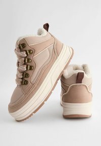 Sneakers da escursionismo beige in mesh e suede, con occhielli dorati, suole bianche spesse e linguetta marrone sul retro, parte superiore testurizzata.
