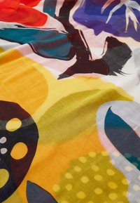 Écharpe colorée présentant des motifs floraux, avec des tons jaunes, bleus et rouges. Fabriquée à partir d'un tissu léger avec une texture lisse.