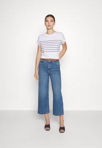 White t-shirt with navy horizontal stripes and a sun graphic, paired with blue wide-leg jeans and black sandals with a knot detail.