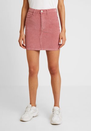 Rosa Denim-Minikleid mit vorderen Knopfverschluss und Taschen, mit strukturierter Oberfläche und geradem Schnitt, kombiniert mit weißen Sneakers.