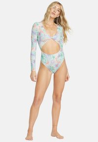 Maillot de bain à manches longues de couleur vert clair avec des motifs floraux en rose et orange. Il présente un design découpé et un décolleté en V.