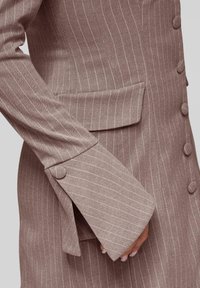 Veste tailored à rayures brunes avec un col cranté, une poche plaquée et des poignets boutonnés en tissu texturé.