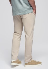 Beige joggingsbroek met zakken, slim fit, van katoen, gecombineerd met lichtbruine sneakers. Gedragen met een mintgroen shirt.