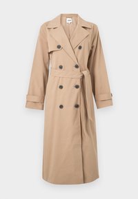 Trench-coat beige à double boutonnage avec boutons noirs, larges revers, manches longues, ceinture à la taille et bracelets aux poignets, suspendu devant un fond blanc.