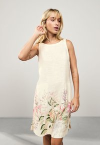 Robe beige sans manches avec des motifs floraux en couleurs pastel à l'ourlet. Confectionnée dans un tissu léger, présentant une surface légèrement texturée.
