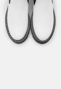 Botines de cuero blanco hasta el tobillo con punta redonda, suela negra y costuras decorativas a lo largo del borde. Las aberturas laterales mejoran la transpirabilidad.