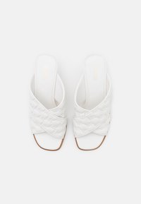 Bílé klouzací sandály s prošívaným designem pásku a otevřenou špičkou. Hladká kožená materiál s mírným podpatkem a hnědými akcenty na podešvi.