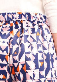 Jupe à motifs colorés mettant en avant des formes géométriques dans des tons de bleu marine, rose et orange. Tissu léger avec une taille élastique pour plus de confort.