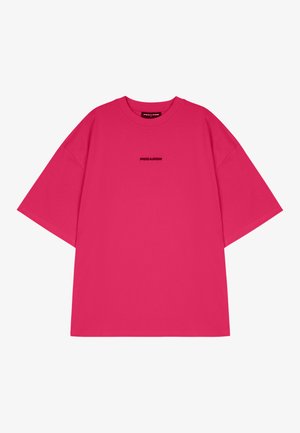 Jasne ružové oversized tričko vyrobené z bavlny. Krátke rukávy, okrúhly výstrih, s malým čiernym logom na prednej strane.