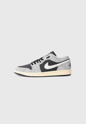 Low-Top Sneaker aus grauem und schwarzem Wildleder mit weißem Nike-Swoosh und schwarzen Schnürsenkeln auf heller Sohle vor grauem Hintergrund.