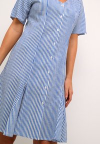Abito a righe blu e bianche, con scollo a V, maniche corte, chiusura a bottoni sul davanti e gonna svasata per una vestibilità comoda. Tessuto leggero.