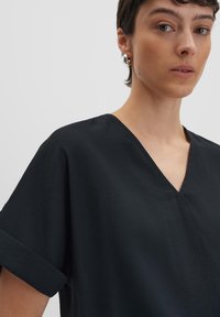 Top nero a maniche corte con scollatura a V, realizzato in un tessuto leggero e testurizzato, con maniche arrotolate e un fit rilassato.