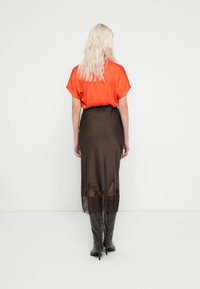 Orange satin top with rolled sleeves, paired with a brown satin skirt featuring a lace hem. Model in knee-high black boots.