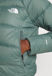 Giacca a vento verde con texture trapuntata, dotata di tasca con zip e logo ricamato. Il polsino presenta dettagli elastici per un maggiore comfort.