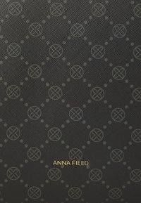 Fekete textúrájú anyag, melyen geometrikus körök és vonalak mintázata található, az "ANNA FIELD" felirattal aranyozva.