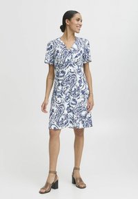 Kratka oblekica z modro-belim paisley vzorcem, z V-izrezom in sproščenim krojem. V kombinaciji s svetlo rjavimi sandali na blok peti.