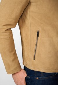 Tan suède jack met een slim fit, met een zijritszak en zichtbare stiksels. Gepaard met donkerdenim jeans.